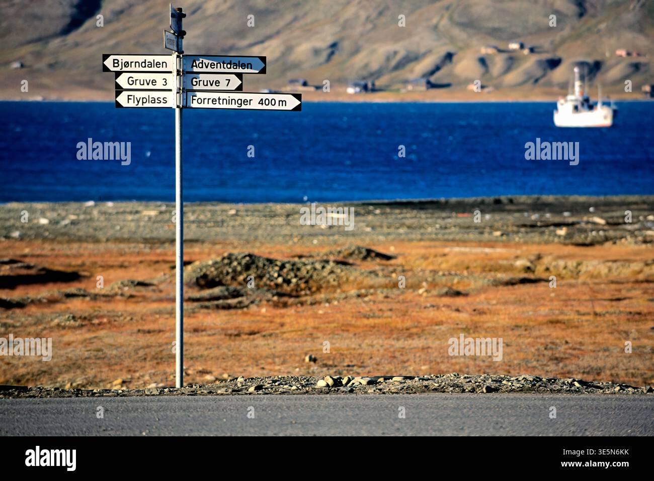 I cartelli stradali mostrano le indicazioni per varie località di Longyearbyen. Il paesaggio artico e l'acqua blu sono sullo sfondo. Foto Stock