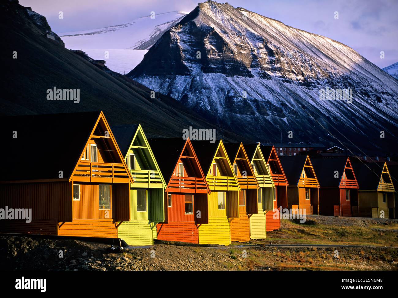 Le cabine dai colori luminosi si trovano ai piedi delle montagne a Longyearbyen, Svalbard. La neve copre le cime mentre la luce del sole tocca le cabine. Foto Stock