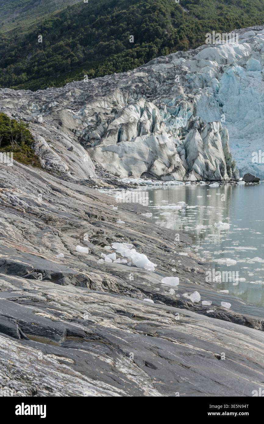 Paesaggio con scintillanti blocchi di detriti di ghiaccio sulla costa rocciosa e le scogliere di ghiaccio del ghiacciaio, girato con la luce brillante dell'estate al fiordo di Pia, in Cile Foto Stock