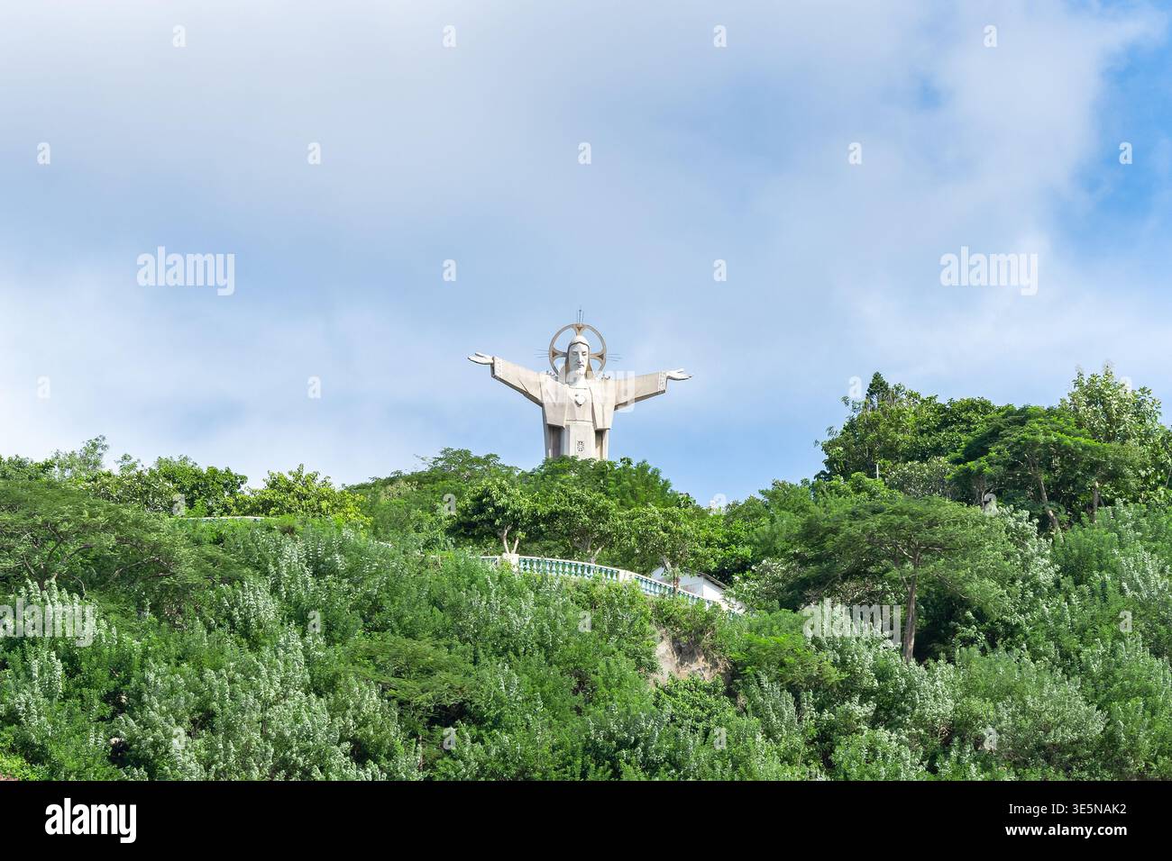 Statua di Gesù Cristo di Vung Tau in piedi sul monte nheo circondato da lussureggianti alberi tropicali verdi contro il cielo nuvoloso primo piano orizzontale Foto Stock