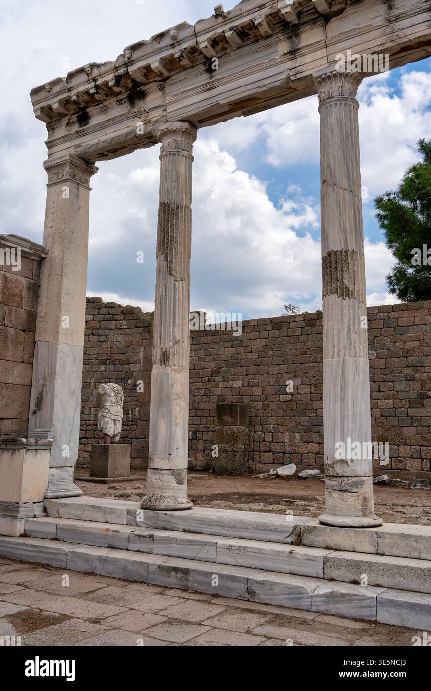 Trajaaneum, le sale, le antiche rovine del tempio romano con colonne maestose e una statua senza testa sotto un cielo nuvoloso a Bergama, Turchia Foto Stock