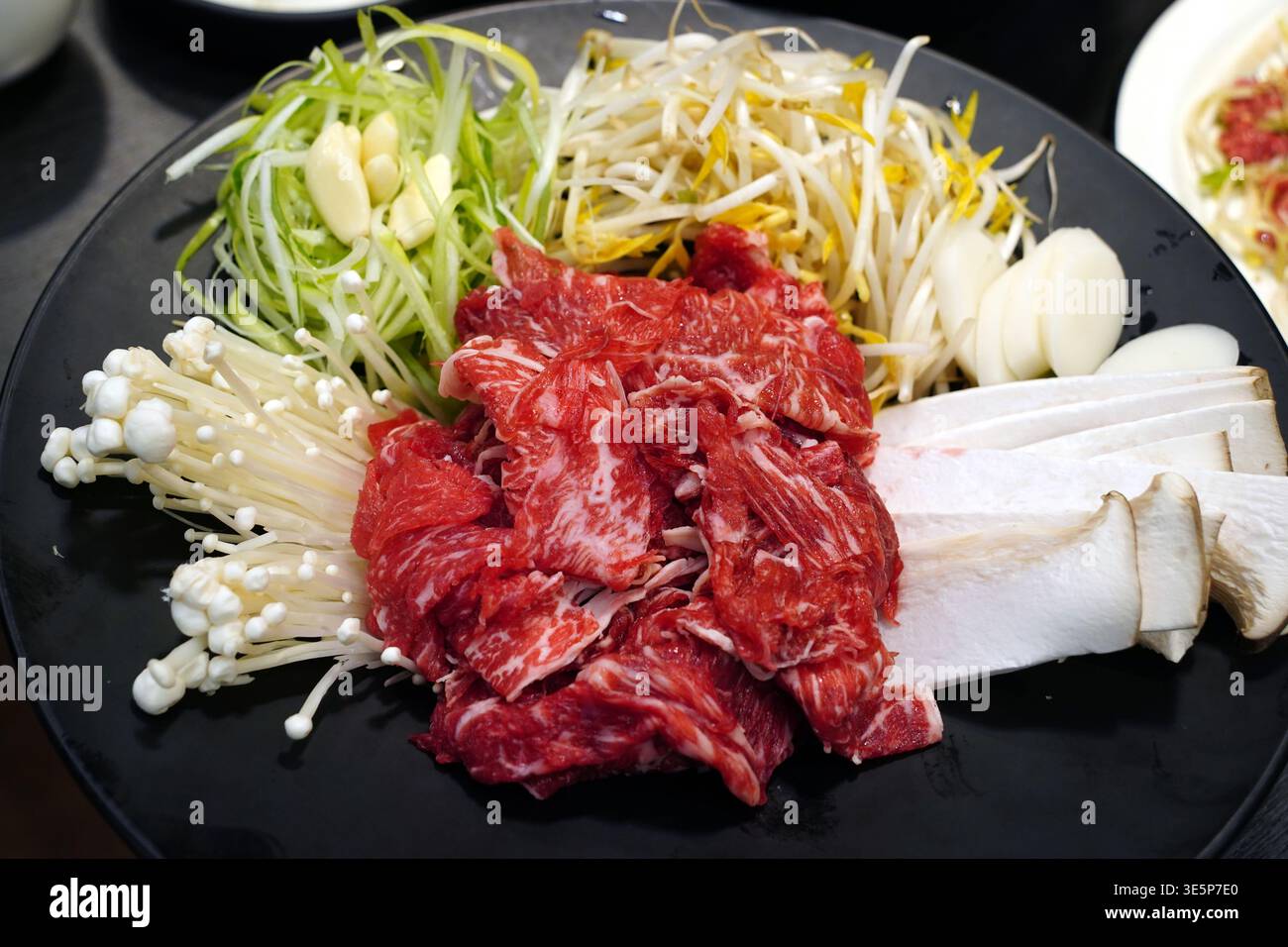 Bulgogi di manzo crudo fresco con verdure assortite, tra cui cipolle verdi, germogli di soia e funghi enoki su un piatto nero Foto Stock