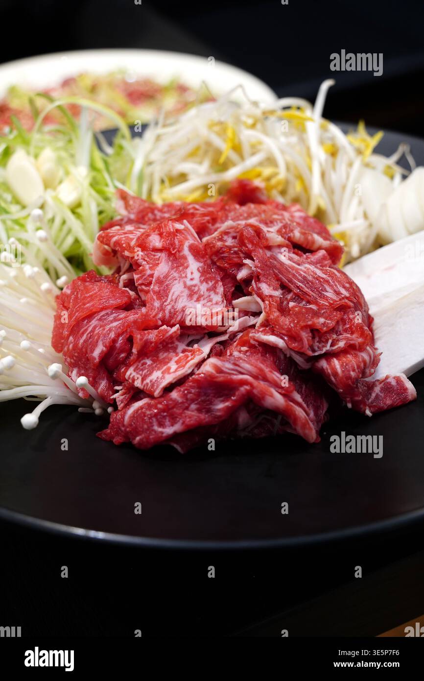 Bulgogi di manzo crudo fresco con verdure assortite, tra cui cipolle verdi, germogli di soia e funghi enoki su un piatto nero Foto Stock