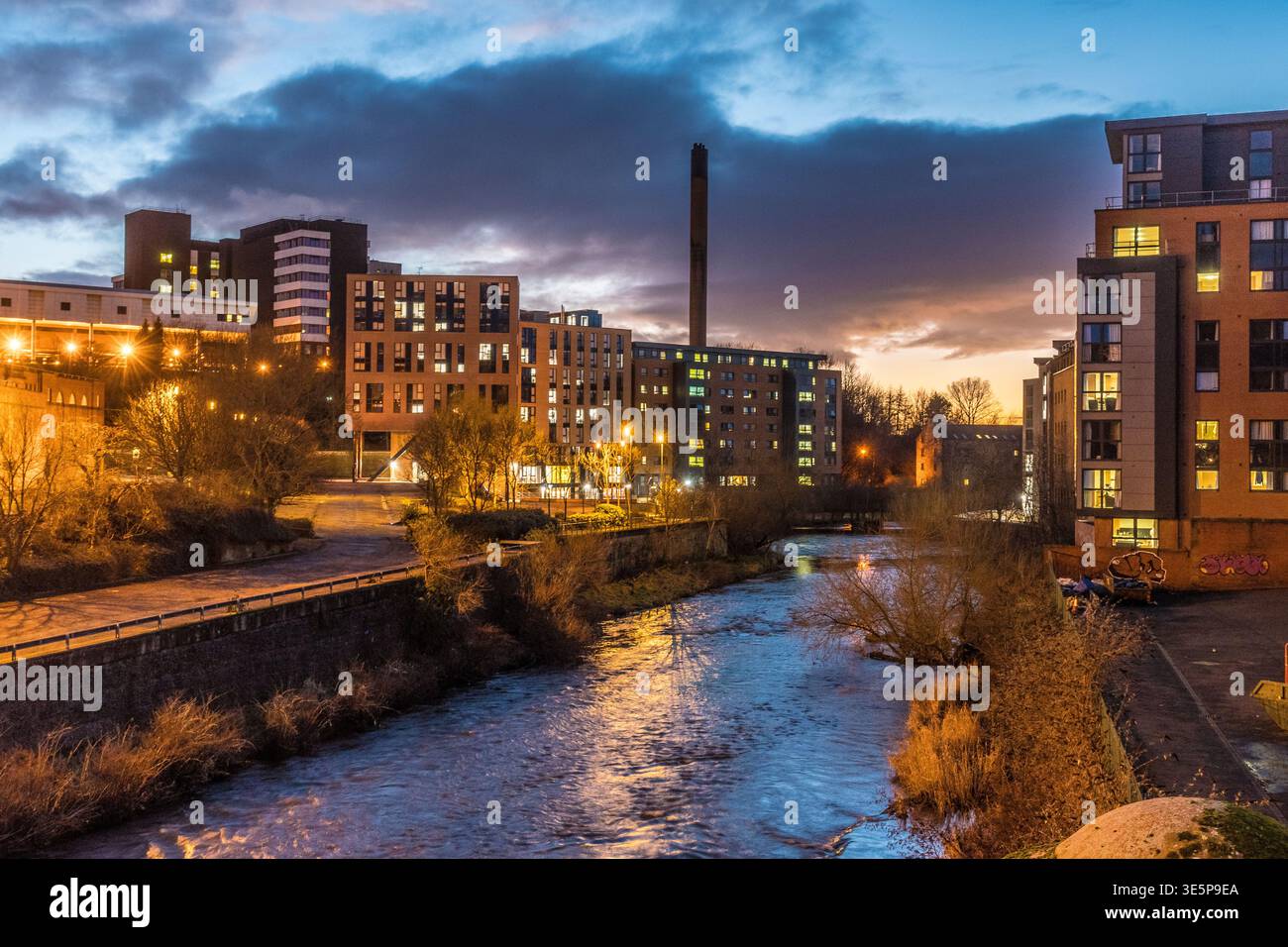 Una vista del fiume Kelvin che scorre oltre la Kelvin Hall al crepuscolo, le luci della città che si riflettono sull'acqua e i moderni appartamenti sul fiume sotto una spettacolare ev Foto Stock