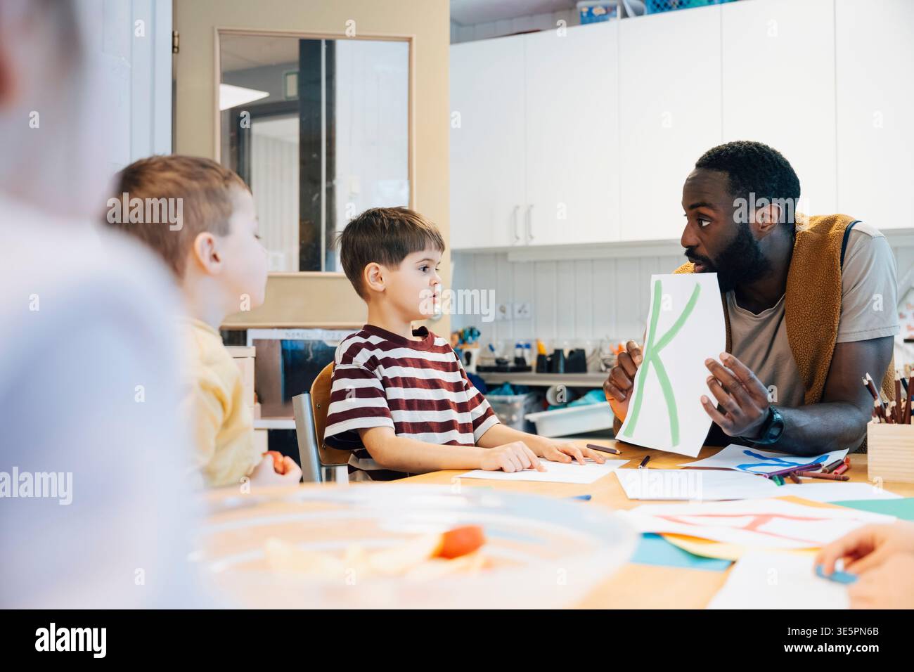 Insegnante di sesso maschile maturo che gioca all'alfabeto creativo con gli studenti dell'asilo Foto Stock