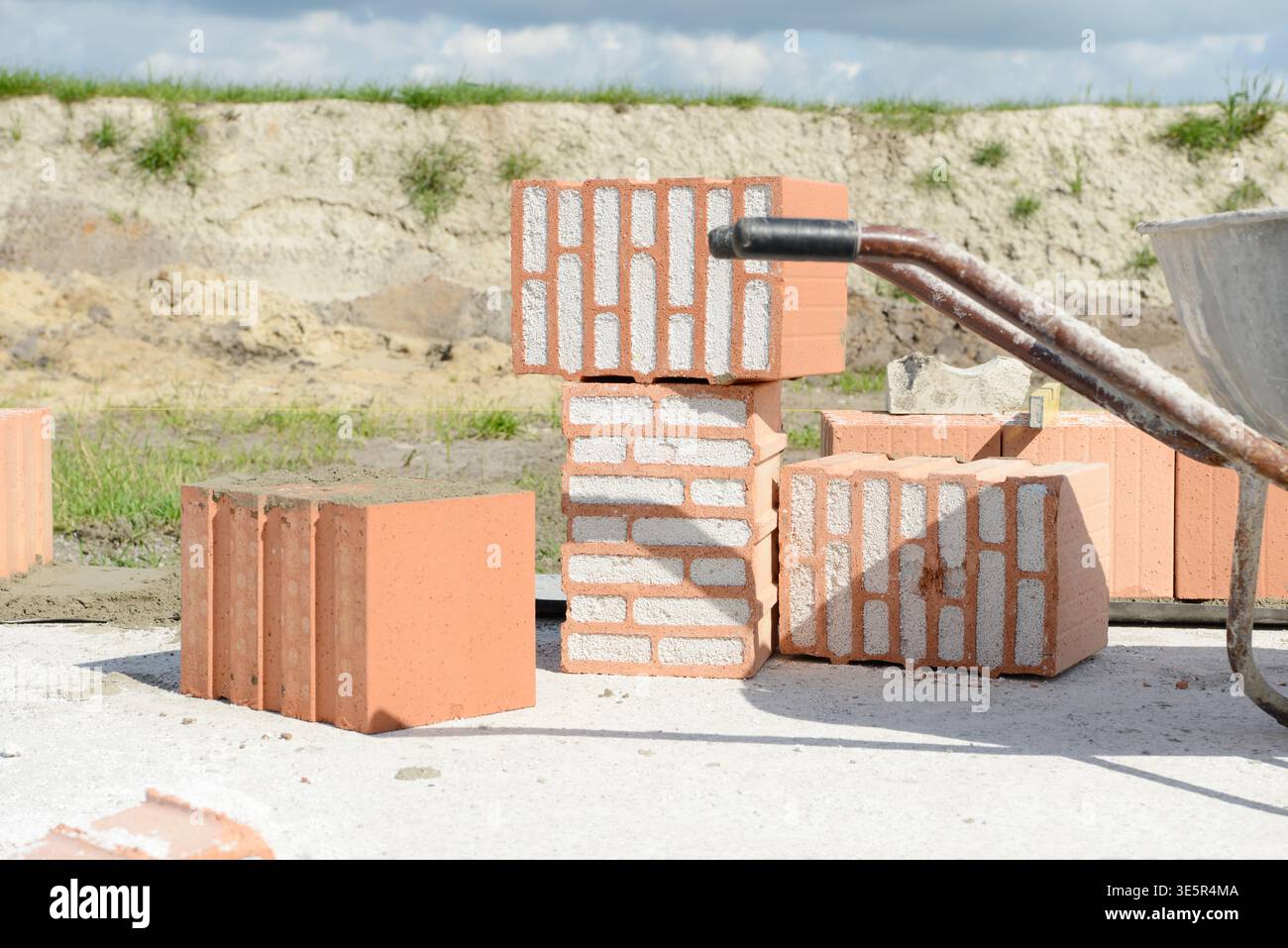 Mattoni di Poroton e carriola su lastre di cemento nel cantiere Foto Stock