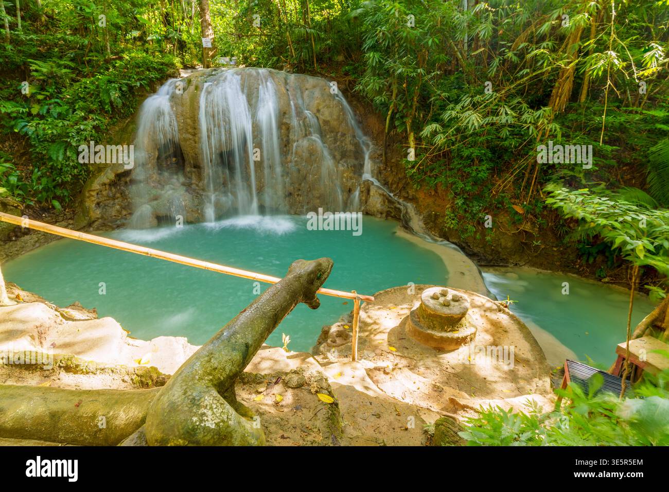 Cascate di Lugnason, Siquijor, Filippine - 16 aprile 2025: Una cascata scorre su una sporgenza rocciosa in una piscina turchese con sculture di roccia. Foto Stock