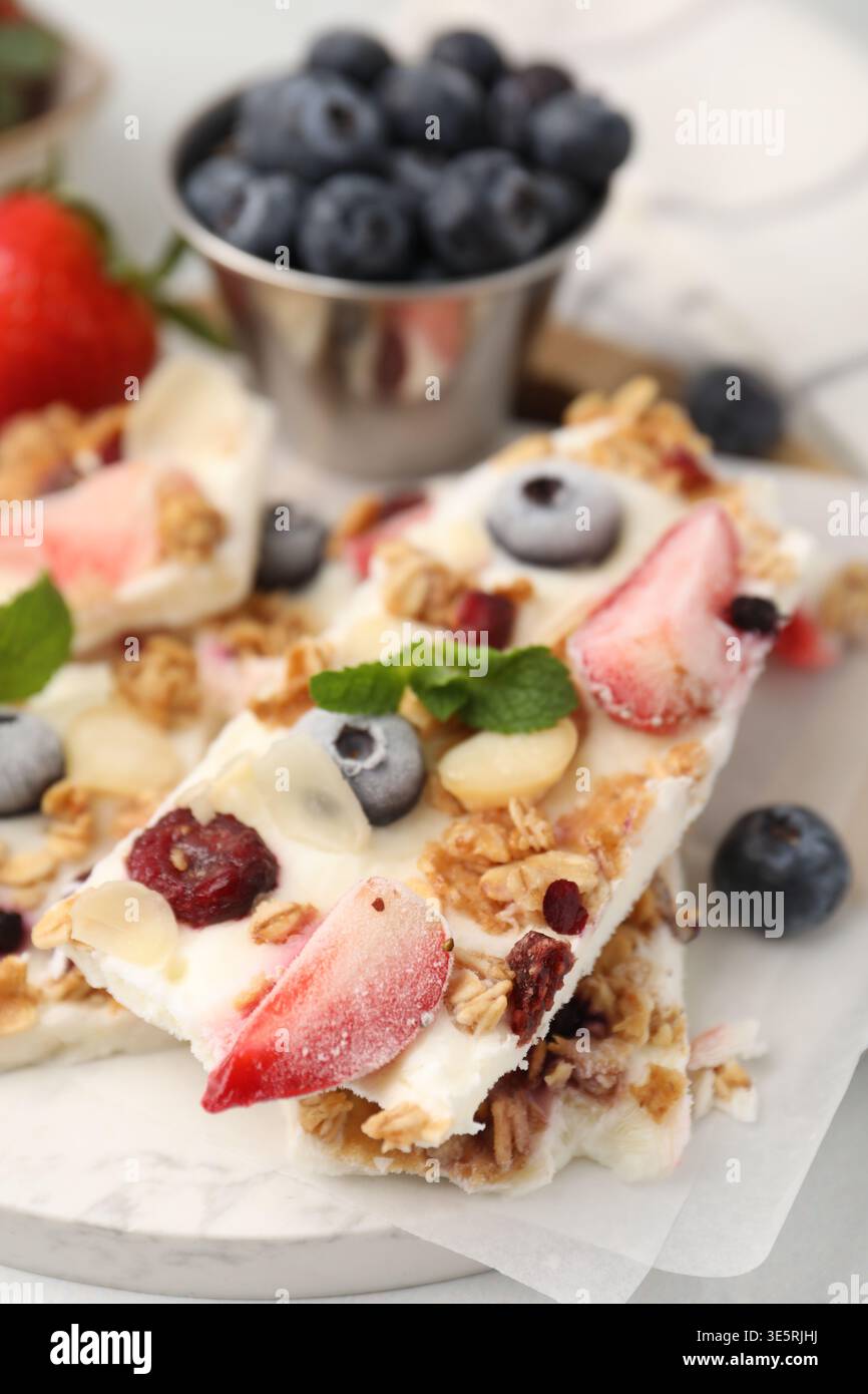 Pezzi di gustosa corteccia di yogurt con frutti di bosco, muesli e menta sul tavolo leggero, primo piano Foto Stock