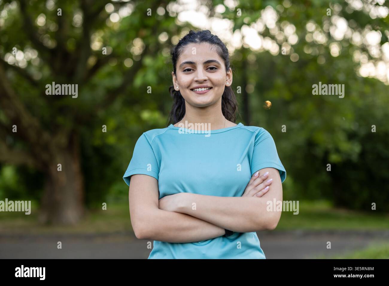 Giovane donna in piedi con sicurezza con le braccia incrociate, sorridente alla macchina fotografica, indossa abbigliamento atletico all'aperto, incarna salute, benessere, e un acti Foto Stock
