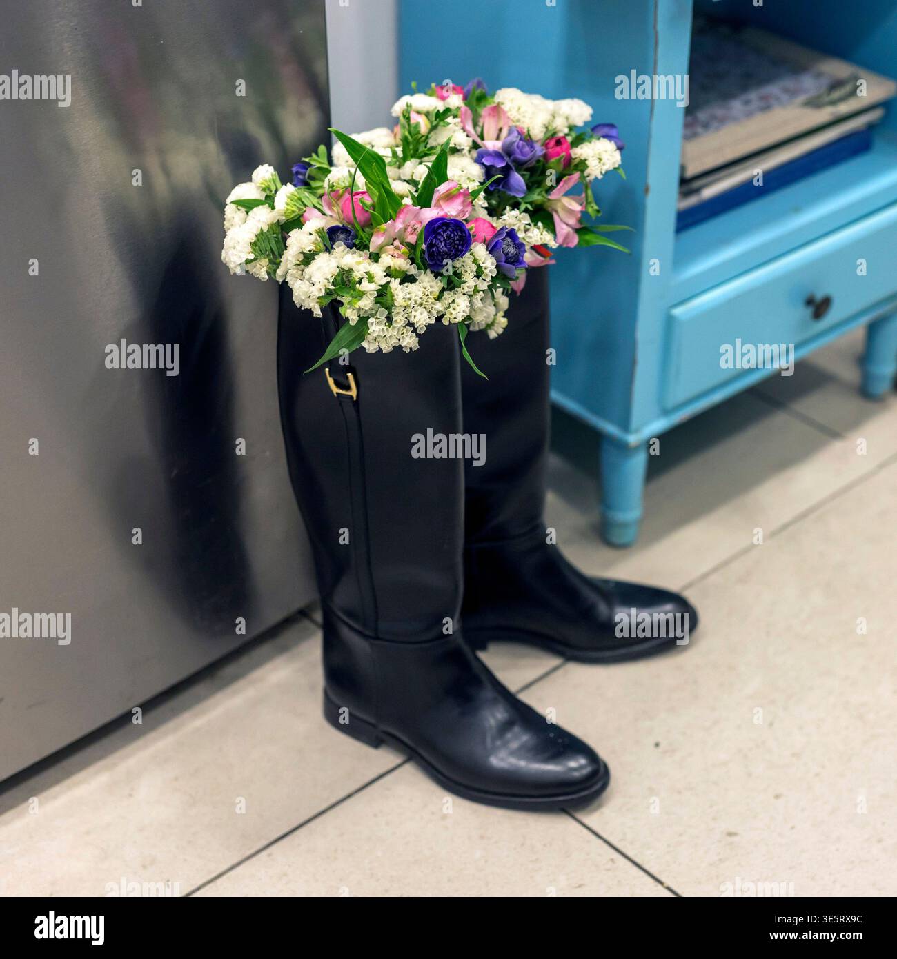 Stivali alti in pelle nera utilizzati come vasi di fiori creativi con un bouquet colorato all'interno. Foto Stock