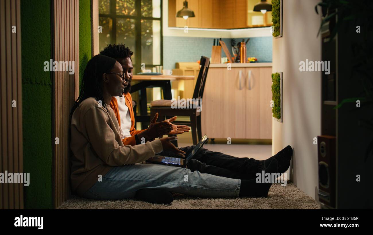 Coppia afroamericana che risolve attività remote sul pavimento, studiando analisi e approfondimenti sui notebook e unendo le forze. Parlare e utilizzare i dati aziendali a casa, aumentare la produttività. Foto Stock