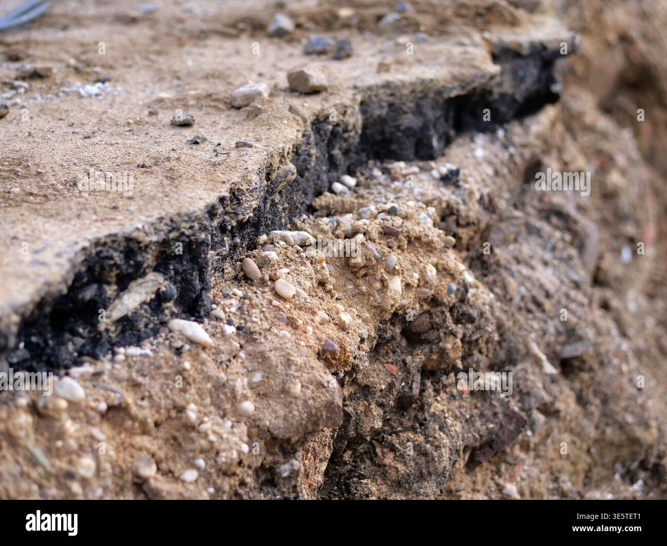 foto ravvicinata del bordo dell'asfalto rotto nel cantiere, sezione trasversale degli strati stradali con bitume nero e base di ghiaia, scavo di opere di terra Foto Stock