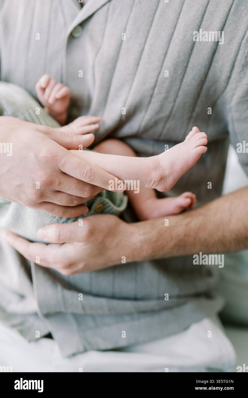 I piedi del bambino abbracciano. Padre Cradles infantile in mano. Il contatto delicato con la pelle simboleggia l'amore e l'intimità della famiglia Foto Stock