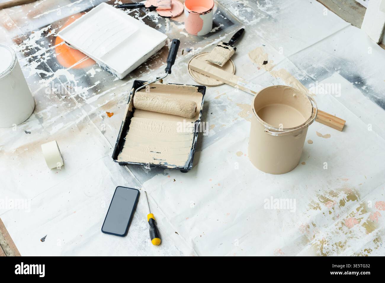 Area di verniciatura su panno che mostra il rullo nel vassoio con barattolo beige, spazzola, cacciavite per telefono con nastro adesivo Foto Stock
