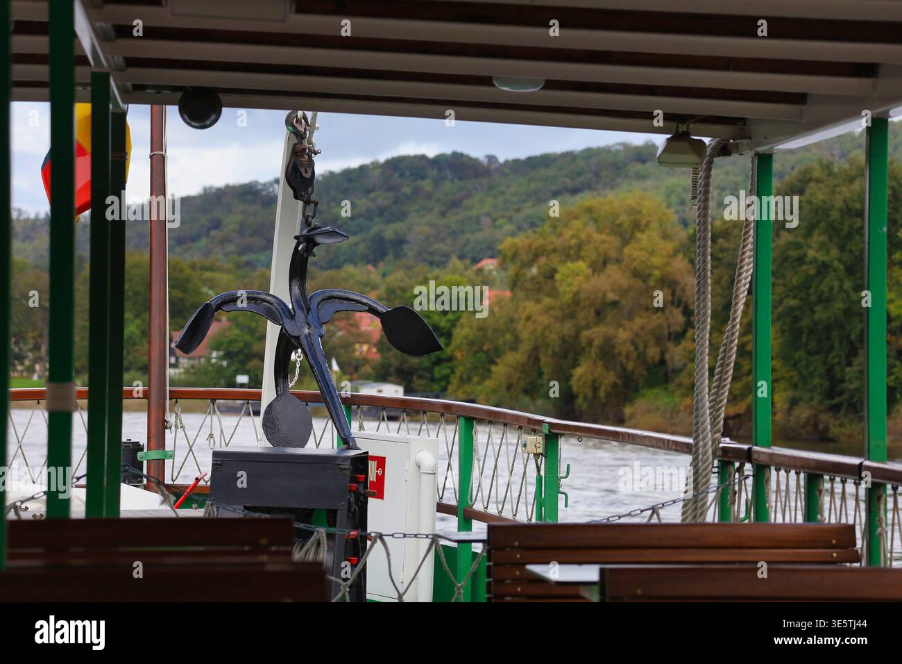 An Bord eines Dresdner Raddampfers: Blick auf den schwarzen Anker am Bug während der Fahrt auf der Elbe vor herbstlicher Uferkulisse Foto Stock