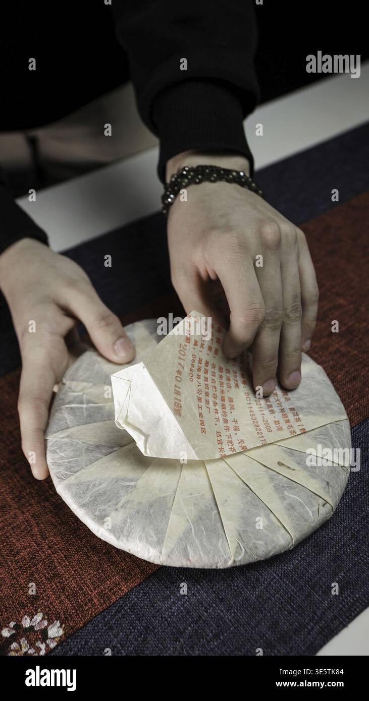 Una vista ravvicinata delle mani che si dispiegano in un tradizionale involucro per la torta del tè, mostrando il suo design elegante e intricato Foto Stock