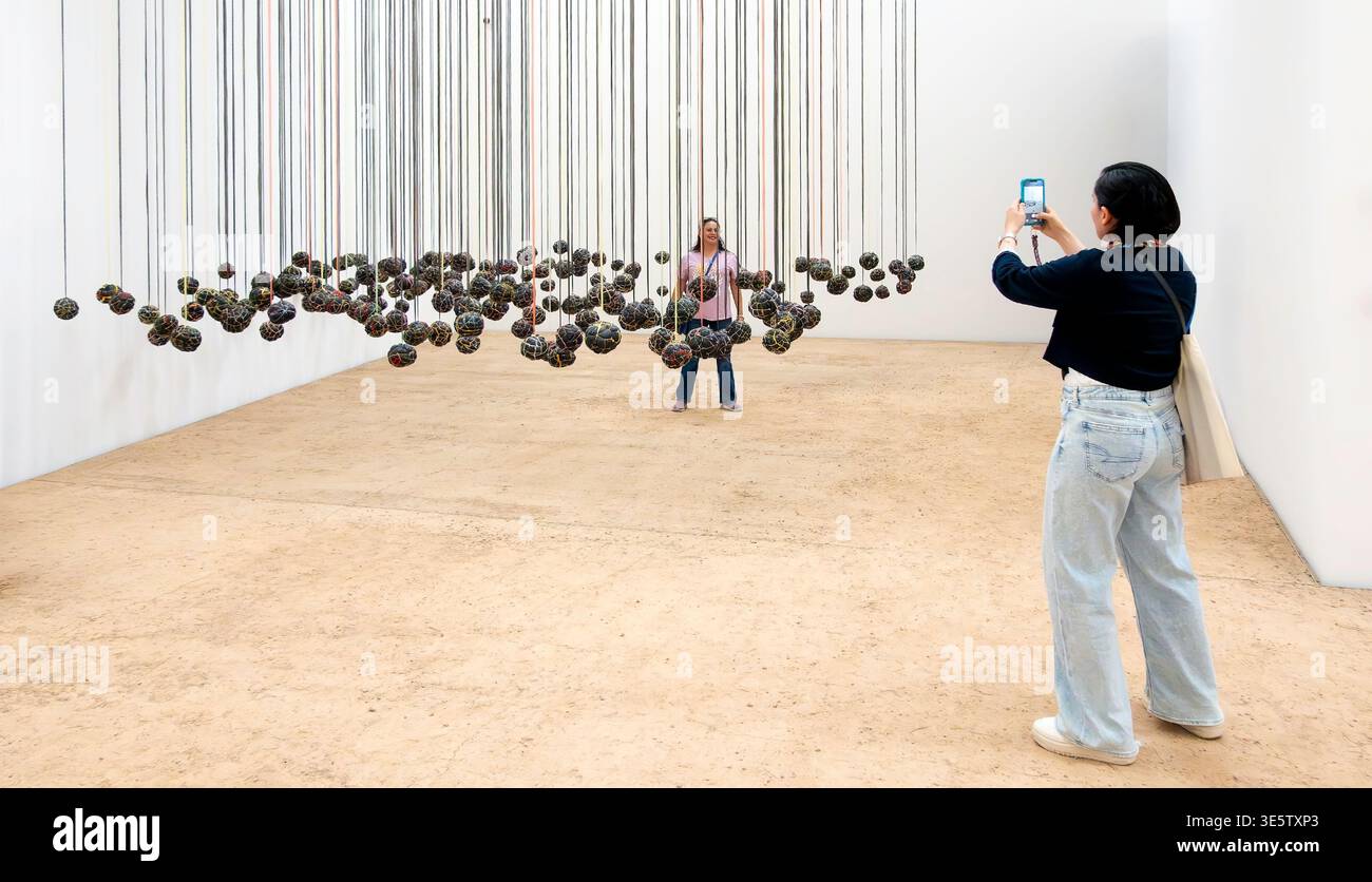 Una donna usa uno smartphone per fotografare un amico nell'installazione artistica sospesa Playtime dell'artista keniota Wangechi Mutu Foto Stock