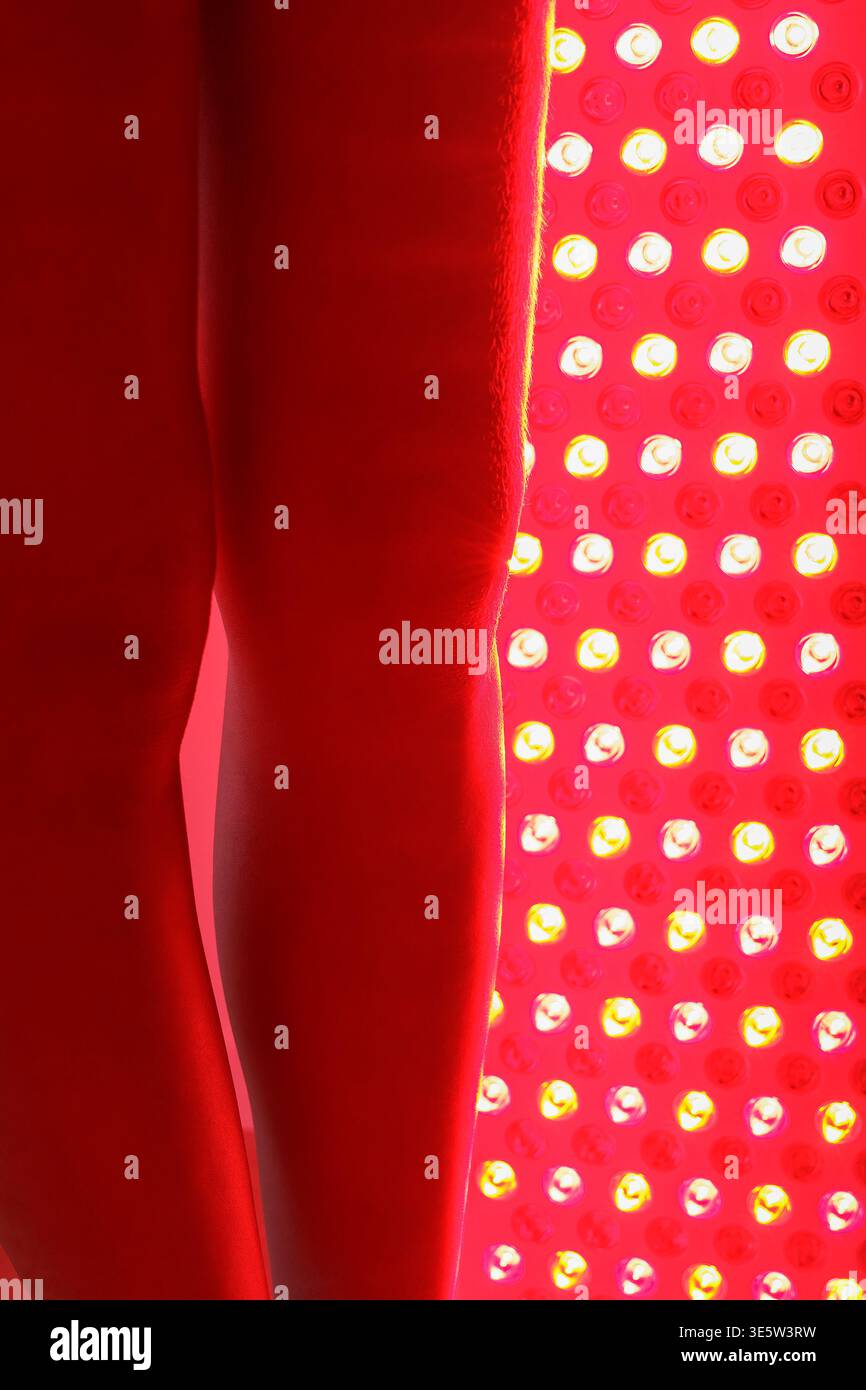 Giovane donna che riceve una terapia a luce rossa sulla parte inferiore del corpo Foto Stock