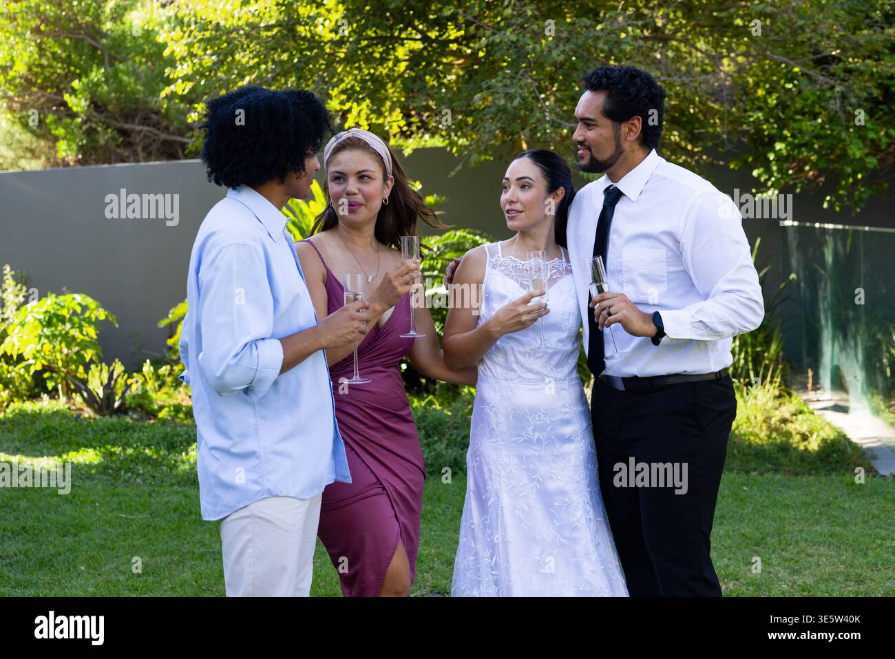 Due coppie con flute di champagne sul prato del giardino, sposa con abito da sposa e fascia Foto Stock