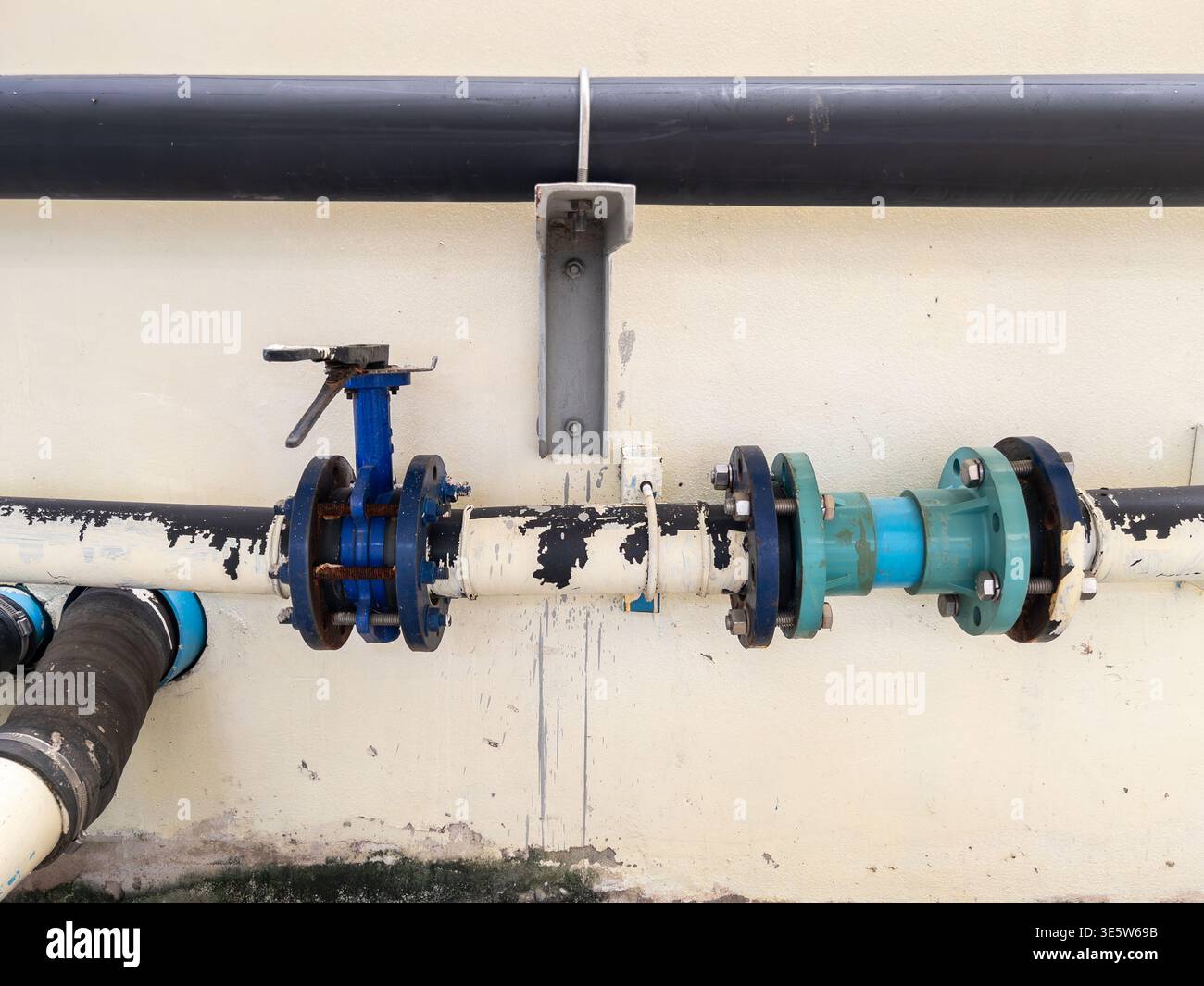 Valvola a farfalla blu industriale e tubi dell'acqua pressurizzati con collegamenti a flangia su parete di una struttura ospedaliera per la gestione delle utenze e delle tubazioni Foto Stock