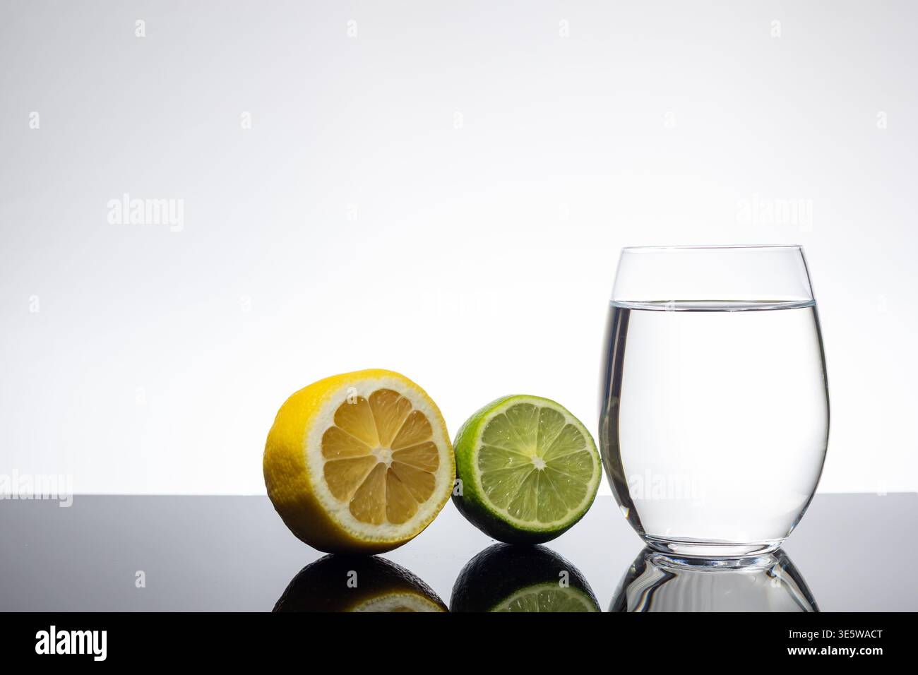 Limone e calce a fette accanto al bicchiere di acqua limpida su sfondo bianco con spazio copia Foto Stock