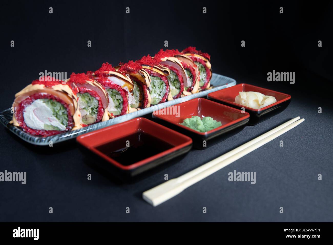 Piatto di sushi roll giapponese gourmet su un piatto di ceramica grigia, condito con maionese piccante, Drizzle e Tobiko rosso, servito con salsa di soia, Wasabi e Pickl Foto Stock