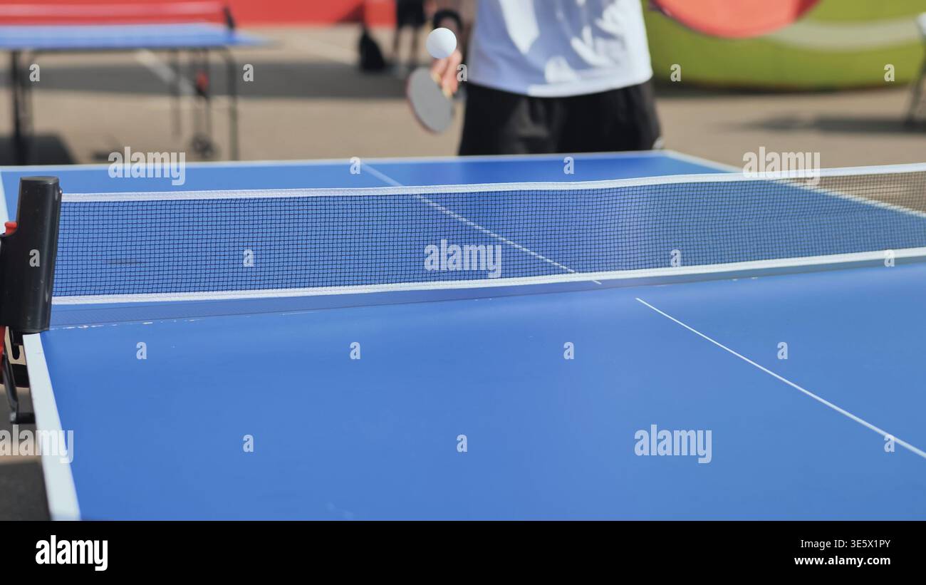 Adulto che gioca a ping pong all'aperto, tenendo il paddle che colpisce palla da ping pong sopra la rete Foto Stock