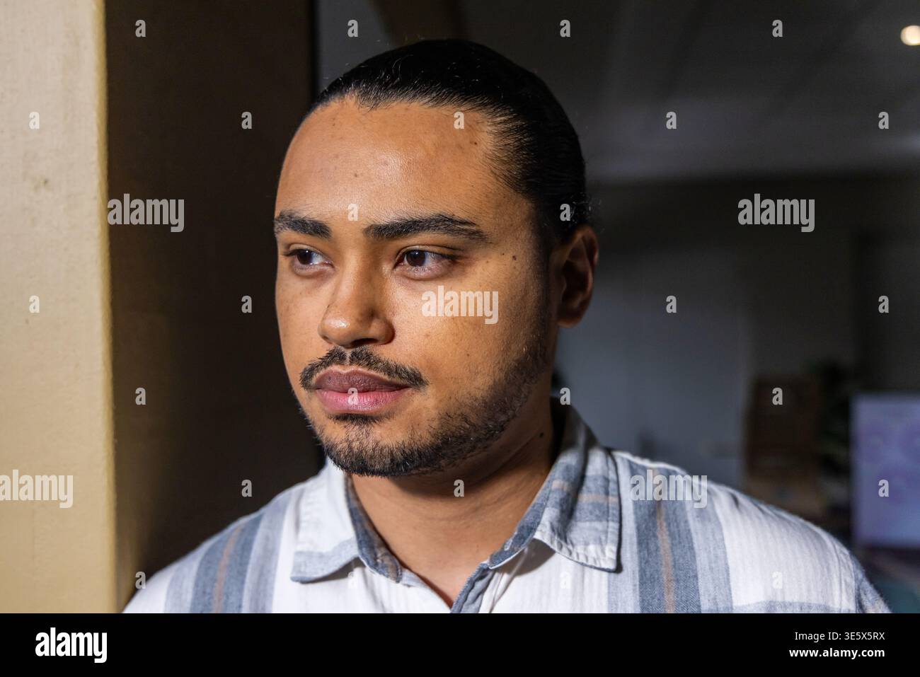 Uomo adulto in piedi vicino alla colonna beige all'interno del soggiorno, con camicia a righe Foto Stock