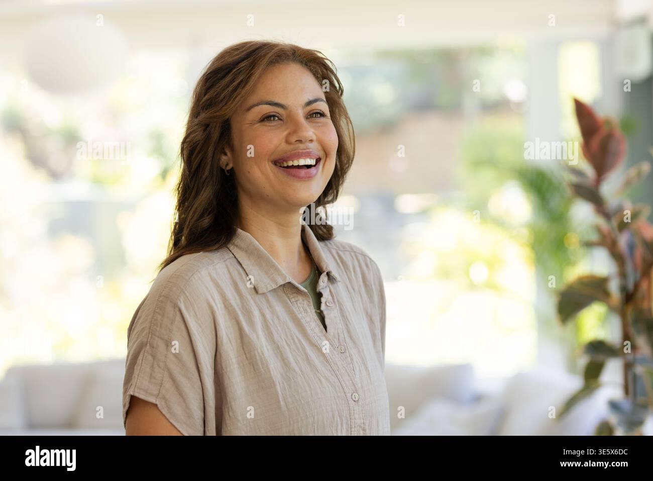 Video verticale: Donna sorridente in cima abbronzata che posa in un luminoso soggiorno, sole che scorre, finestre visibili Foto Stock