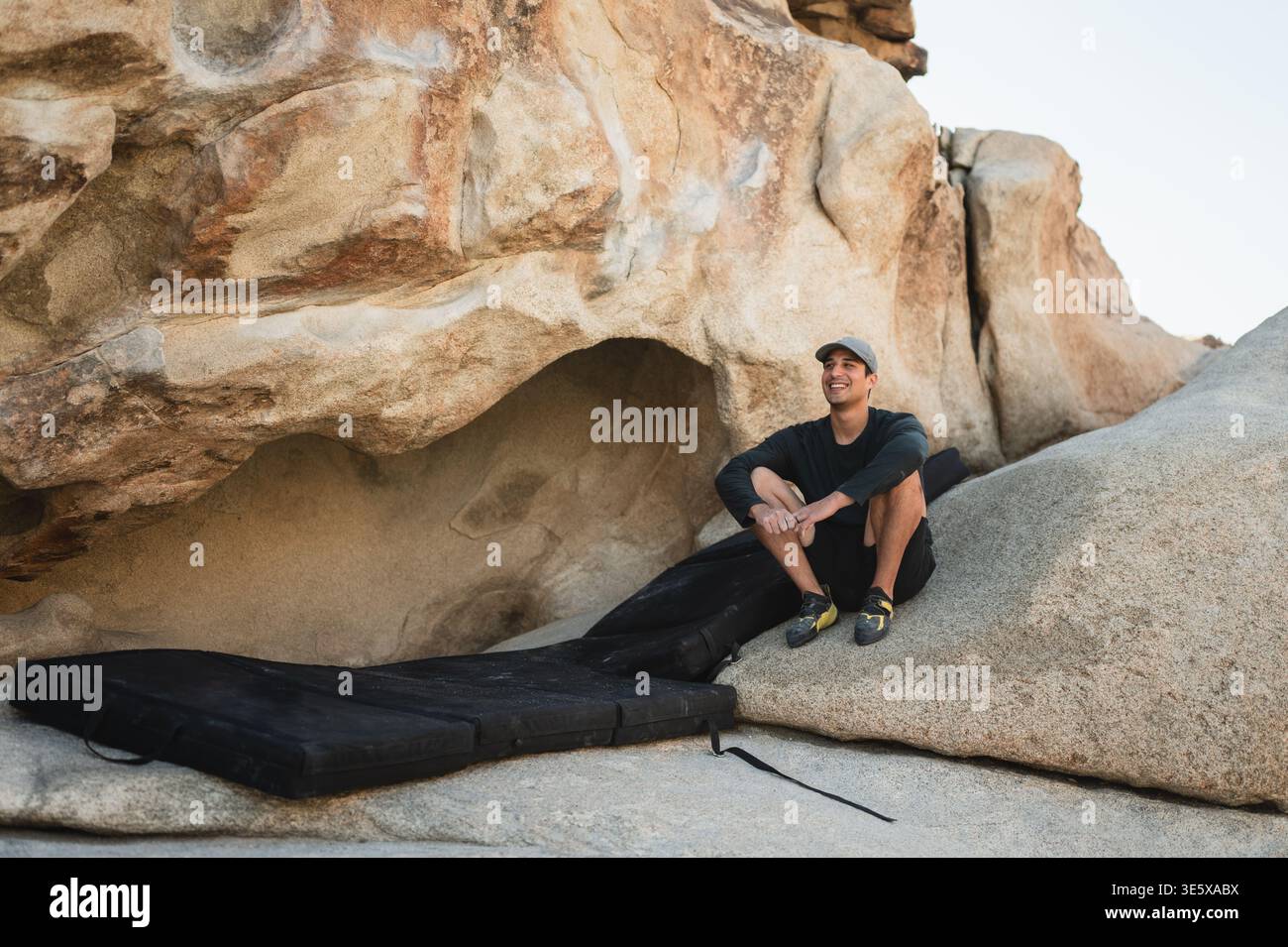 Arrampicatore sorridente che riposa su un masso con blocchi d'urto nel deserto Foto Stock