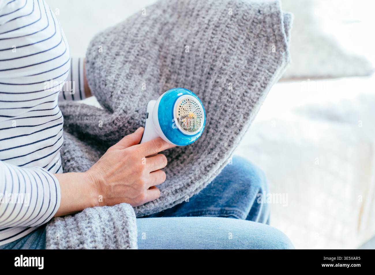 Donna corta che rimuove le pillole dal tessuto a maglia grigio con rasoio elettrico Foto Stock
