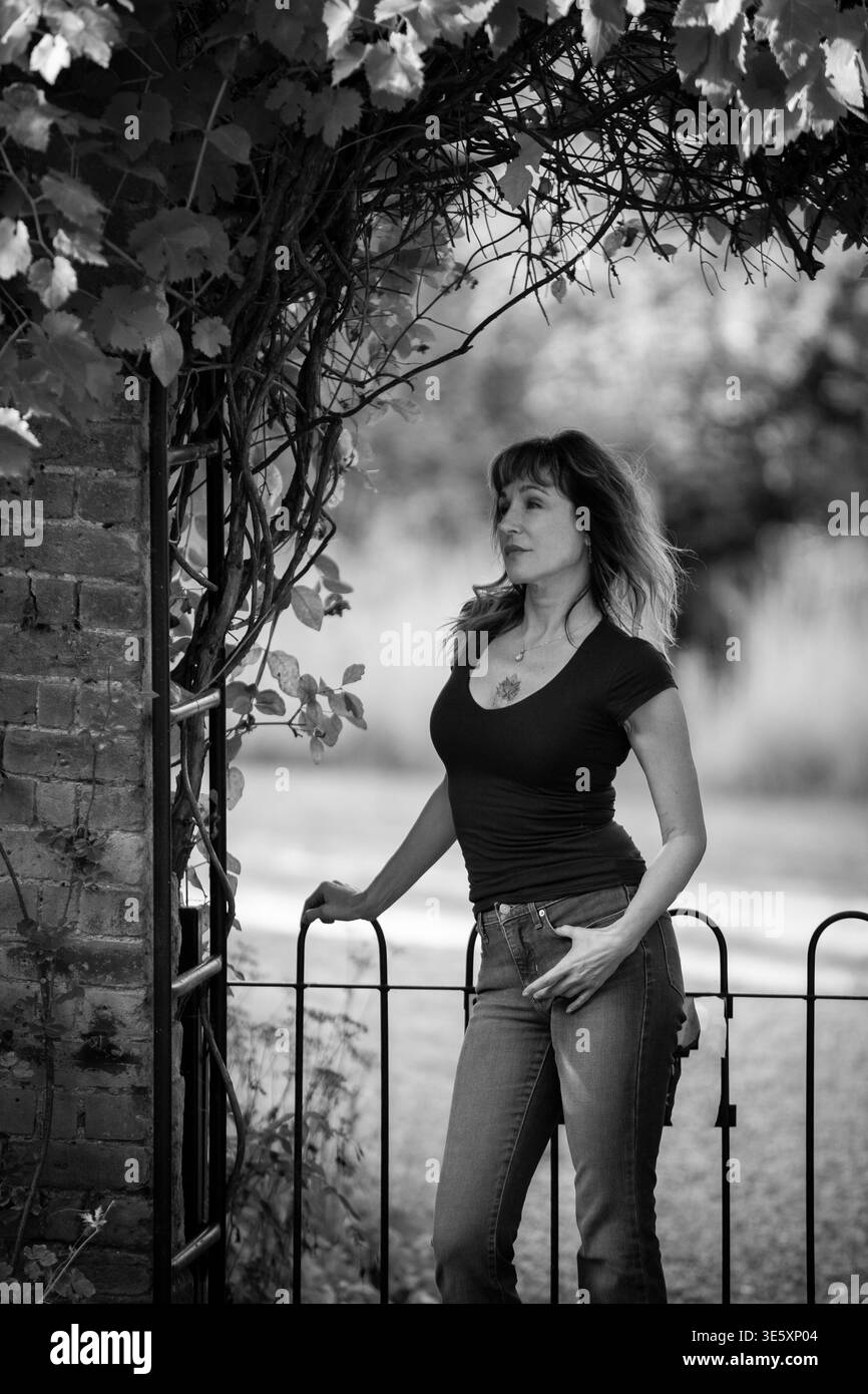 Donna in piedi accanto all'arco e al cancello del giardino, ritratto all'aperto in bianco e nero in un ambiente di campagna Foto Stock