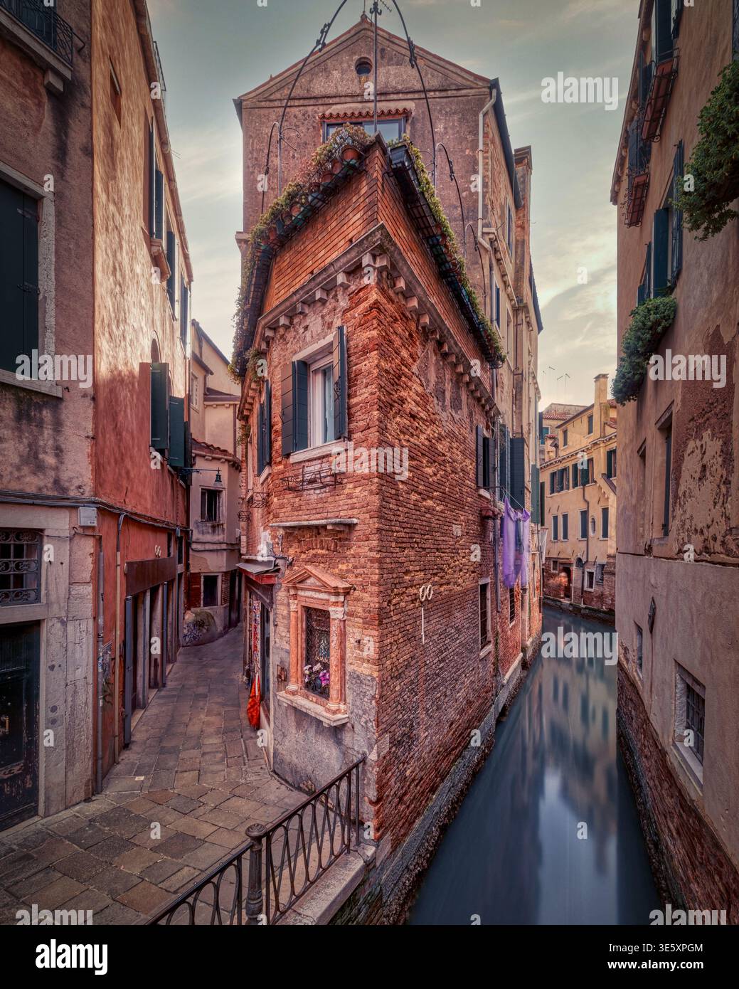 Stretto canale veneziano accanto a case in mattoni e un vicolo tranquillo con la calda luce della sera, Venezia, Italia. Foto Stock