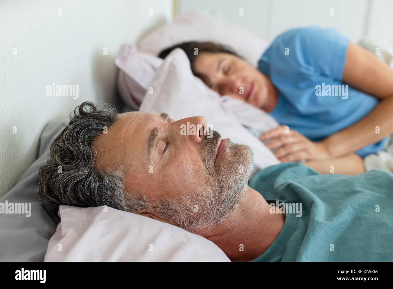 Coppia senior che riposa fianco a fianco sul letto in camera da letto con cuscini, piumone e T-shirt Foto Stock