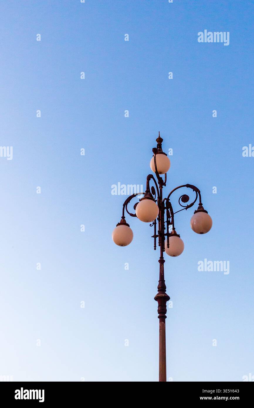 Lampada da strada vintage contro il cielo azzurro con luci a forma di globo ornate al tramonto Foto Stock