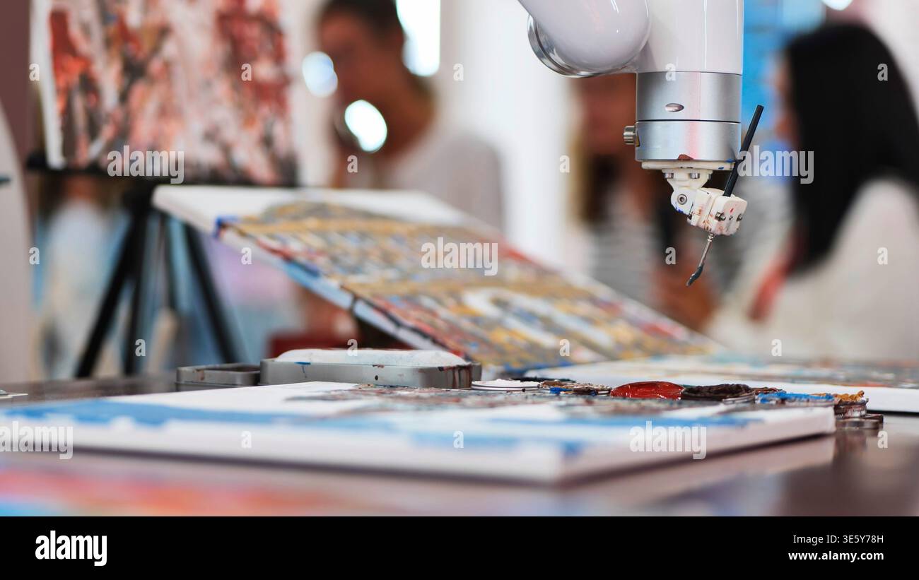 Primo piano di un braccio robot IA che dipinge un quadro astratto su tela in uno studio d'arte Foto Stock