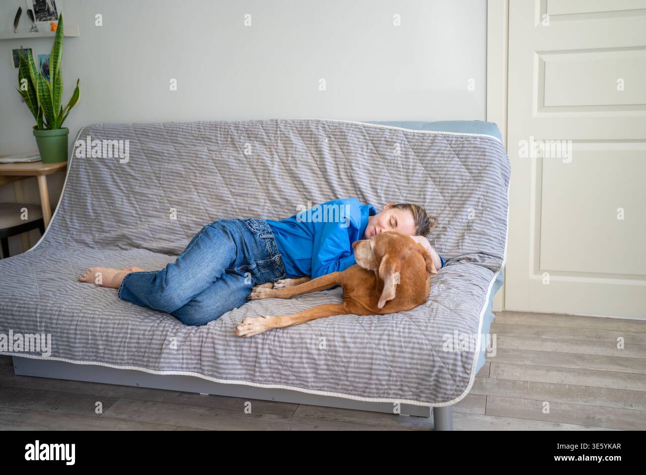 Amore incondizionato per il cane. Una donna rilassata abbraccia dolcemente il cane sul divano. Adozione animale per donna solitaria Foto Stock
