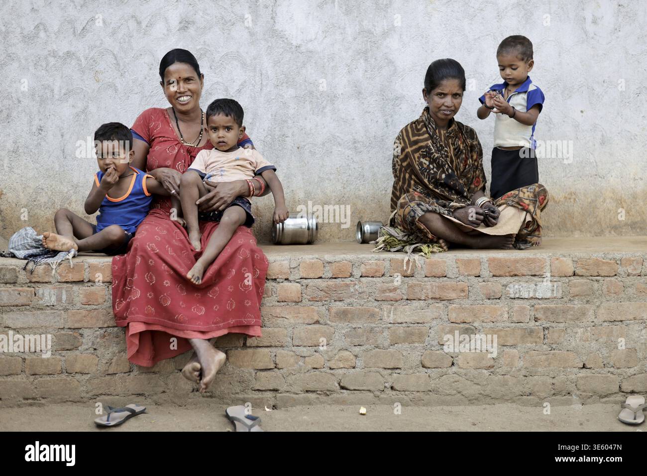 Odisha, India - 26 marzo 2026: Vista di una madre e dei bambini a Odisha, India, i loro abiti vibranti contrastano con i toni tenui del mattone An Foto Stock