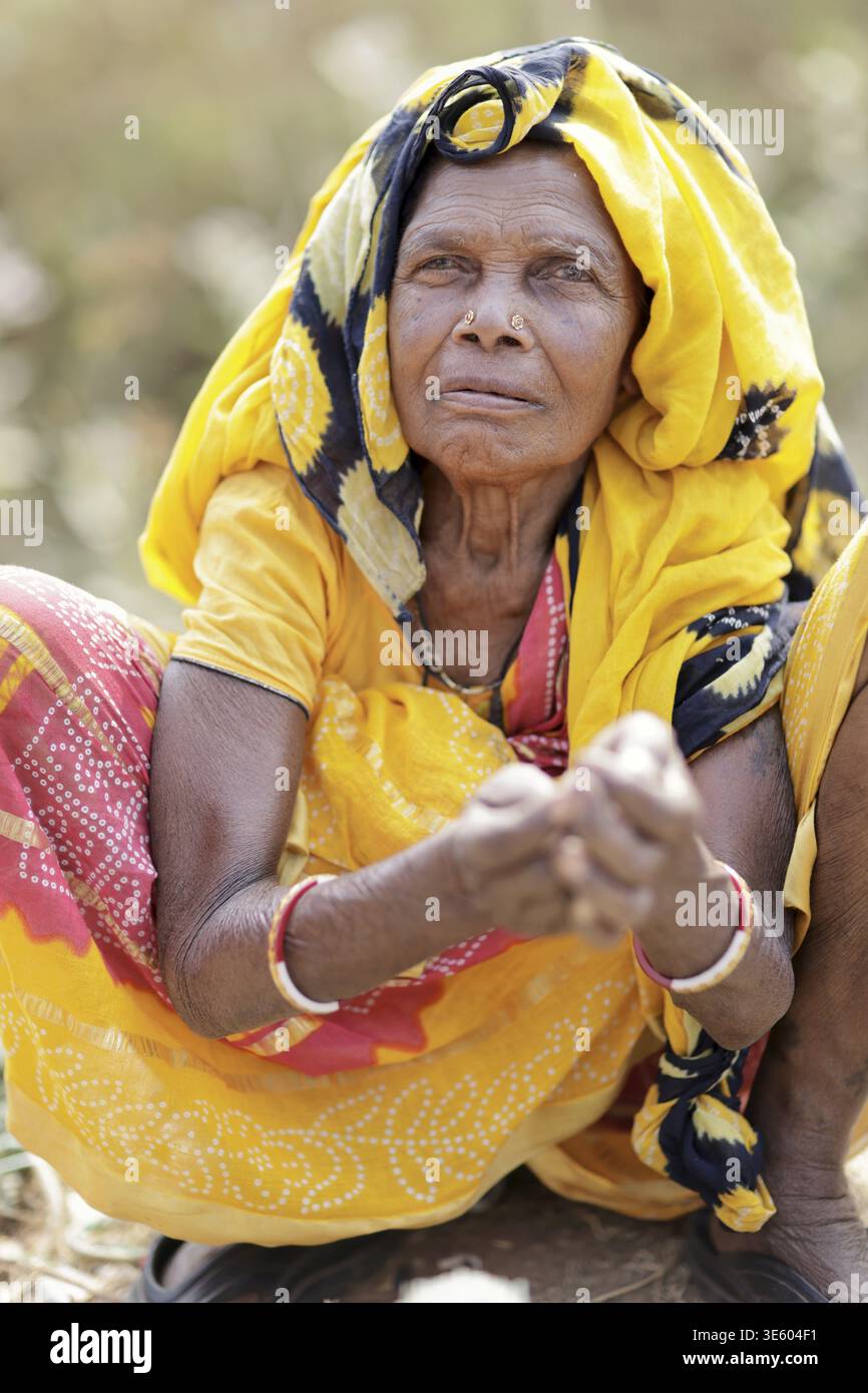 Odisha, India - 26 marzo 2026: Vista di una donna anziana con un velo giallo e braccialetti rossi, le sue mani intemprate stringono, incarnando una vita incisa Foto Stock