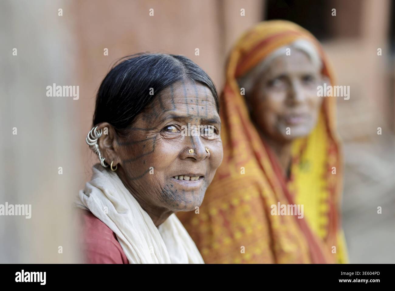 Odisha, India - 26 marzo 2026: Veduta di due donne, una con i tradizionali tatuaggi facciali, i loro volti intemprati che raccontano storie di resilienza contro un bac Foto Stock
