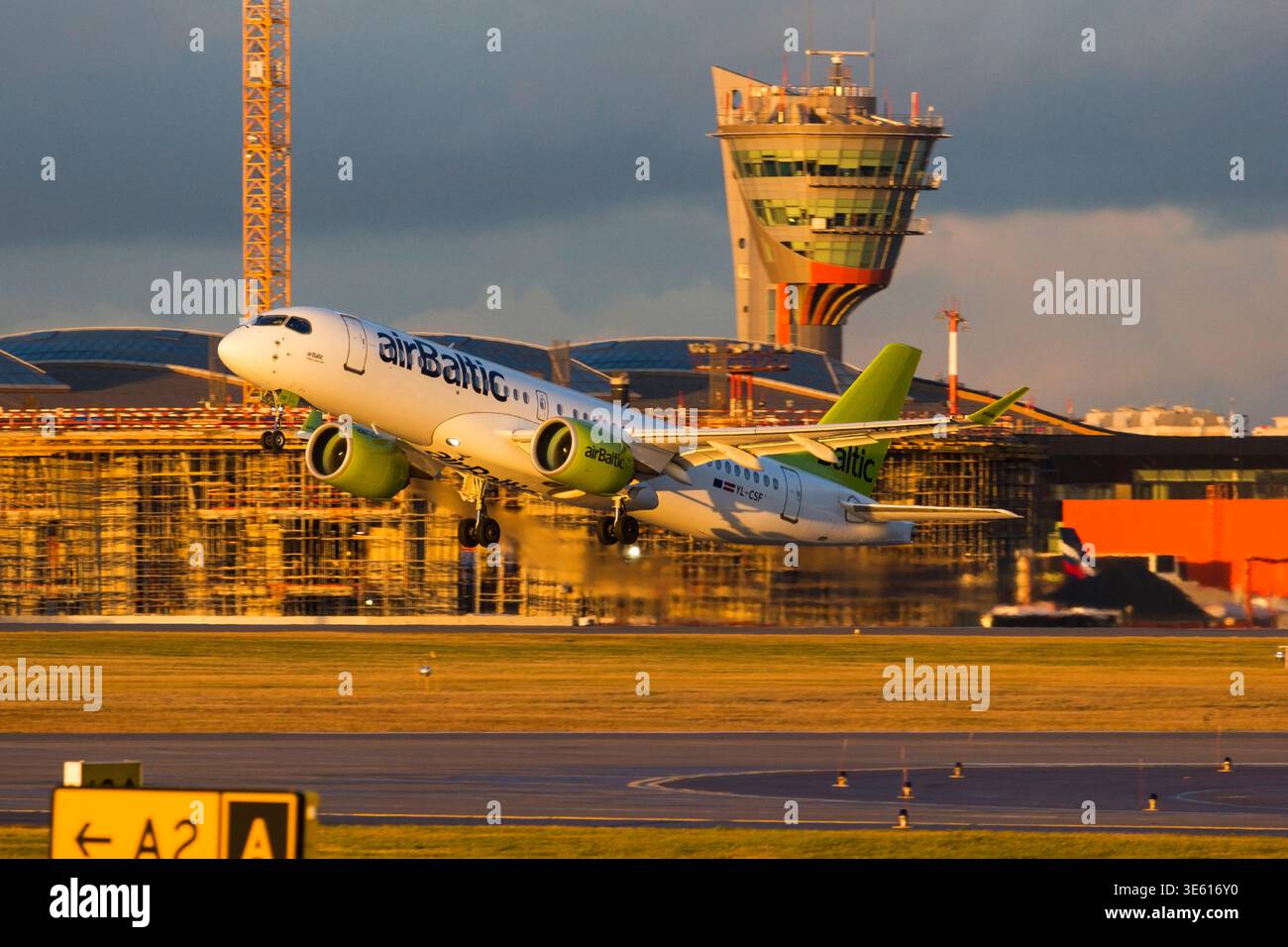 Mosca, Russia – AirBaltic Airbus A220 aereo passeggeri in decollo dall'aeroporto internazionale di Sheremetyevo con torre di controllo sullo sfondo Foto Stock
