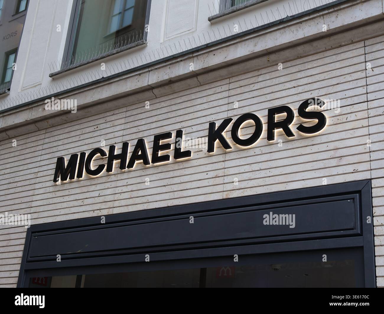 18.01.2026 Monaco di Baviera: Insegna Michael Kors illuminata montata sopra un'elegante facciata in pietra che segna l'ingresso di una boutique di lusso, che trasmette il marchio Foto Stock