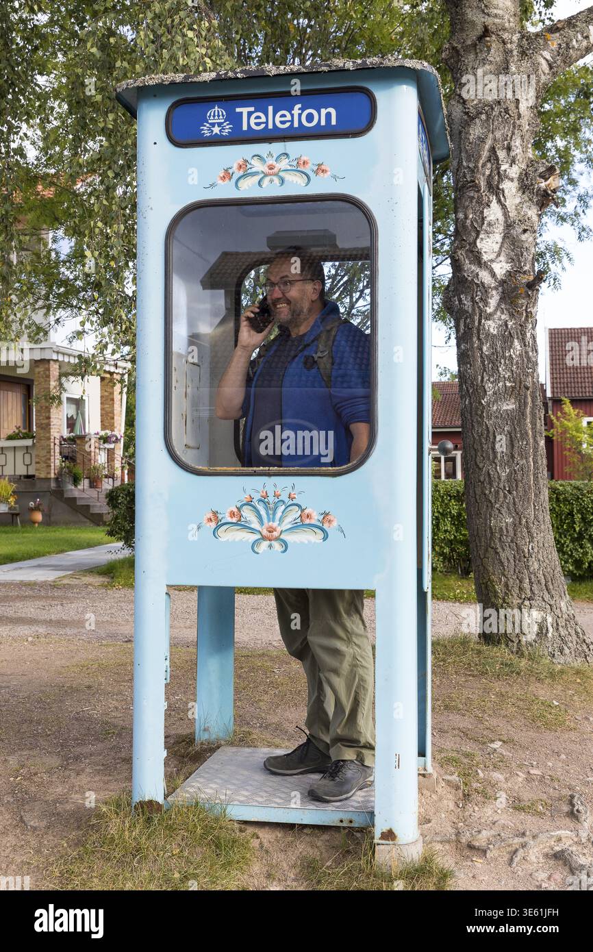 Uomo che fa una telefonata con un cellulare in una cabina telefonica svedese con vernice, ora senza telefono, Nusnaes, Dalarnas laen, Svezia Foto Stock