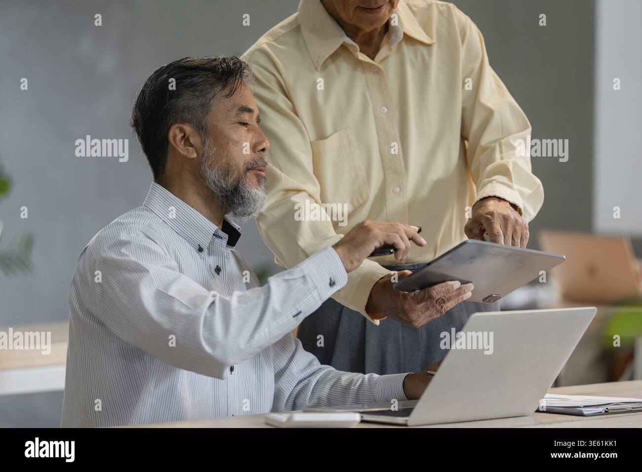 Un signore anziano condivide un tablet con il suo consulente aziendale, sottolineando l'importanza della tecnologia nelle pratiche aziendali moderne Foto Stock