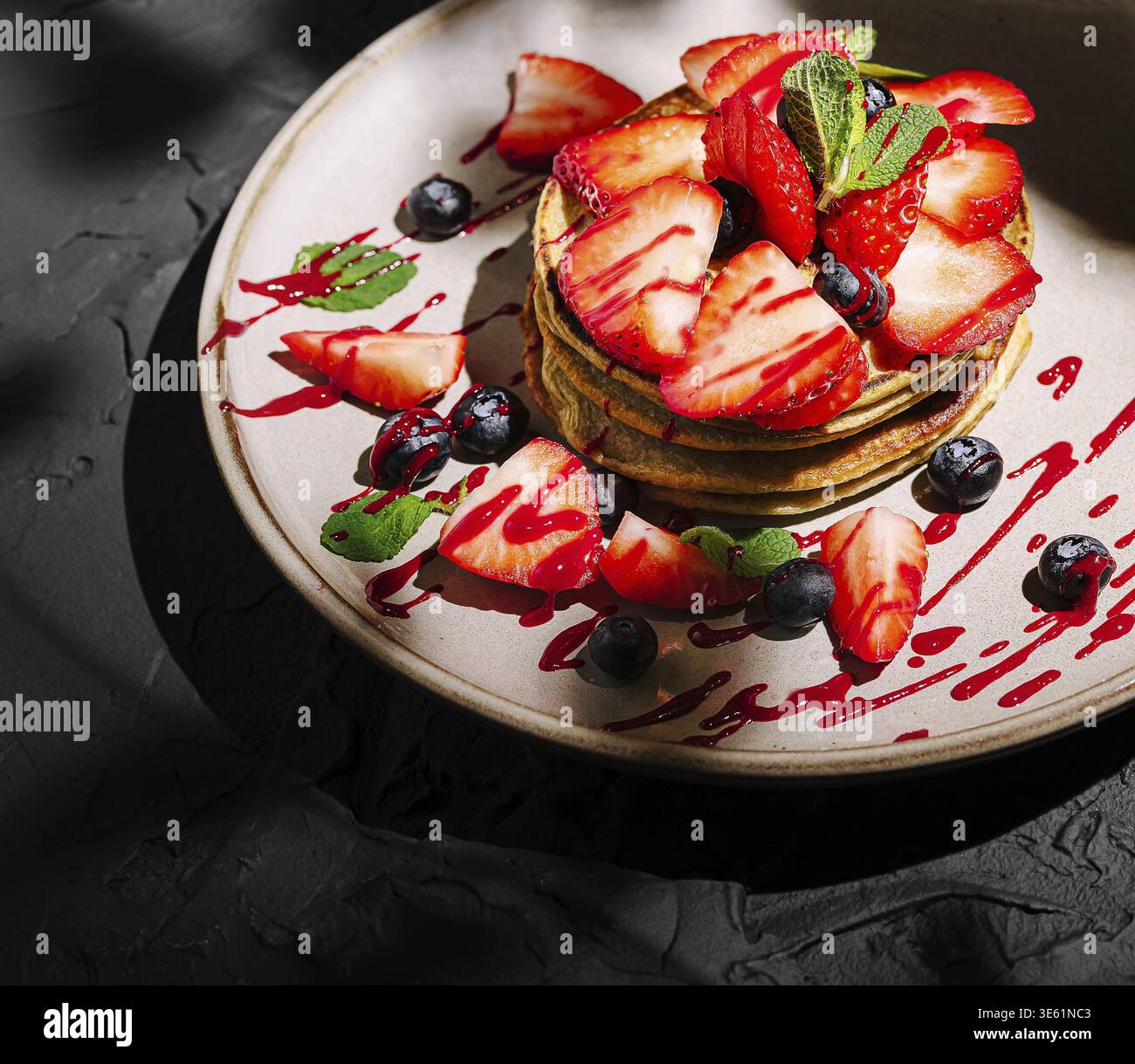 Il cibo, i pancake alti sono impilati artisticamente su un piatto, adornati con fragole a fette, mirtilli e un filo di salsa di bacche, adornati con un da Foto Stock