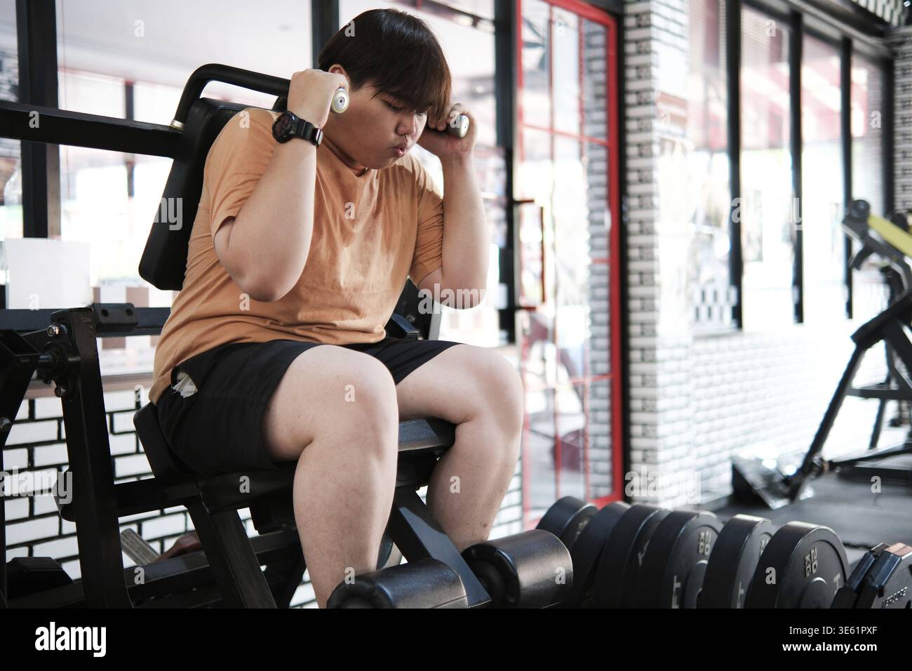 Grasso asiatico uomo che gioca con attrezzature fitness per perdere peso in palestra Foto Stock