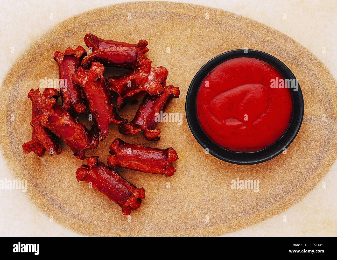 Cibo, spuntini salati colorati a forma di ossa sono disposti in modo ordinato, accompagnati da una piccola ciotola di salsa piccante rossa su una platte di legno testurizzato Foto Stock