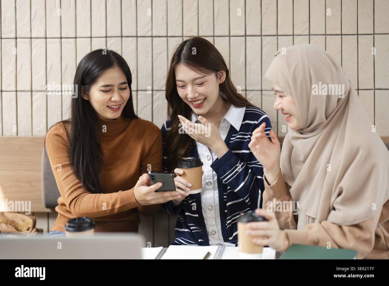 In un ambiente rilassato, tre amici del college condividono una risata mentre esaminano alcuni contenuti su uno smartphone, arricchendo la loro esperienza di apprendimento Foto Stock