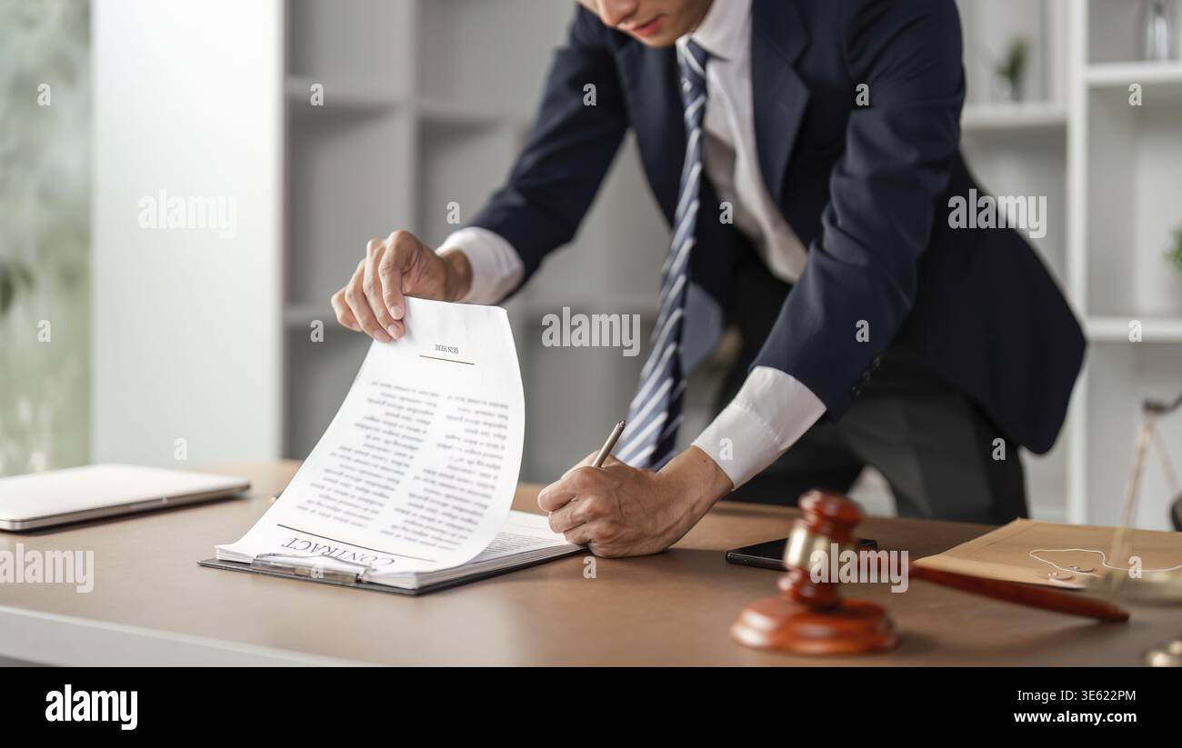 Un giovane avvocato asiatico sta esaminando e firmando i documenti contrattuali legali presso la sua scrivania, dedicata al suo studio legale Foto Stock