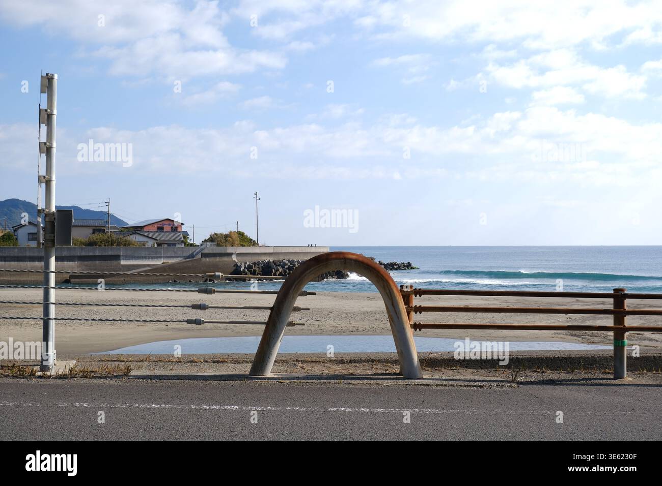 Barriera costiera lungo la strada con un grande arco di tubi in acciaio arrugginito e un palo di avvertimento che si affaccia su una barra di sabbia e sull'Oceano Pacifico, Miyazaki, Giappone. Foto Stock